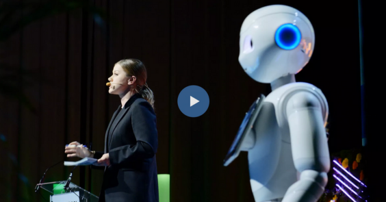 Picture of a human and of a robot on a stage during a conference