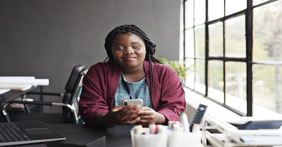 African-American visually impaired woman sitting in an office smiling and looking at the camera 